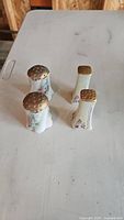 Four vintage ceramic salt and pepper shakers displayed on a table, showing the group arrangement and brass tops.