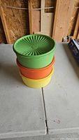 Stacked yellow, orange, and green vintage Tupperware canisters on white table with radiating lid design visible