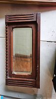 Front view of rectangular wall mirror with brown wooden frame featuring decorative linear slot cut-outs along vertical and horizontal edges. Mirror glass shows signs of age and wear.