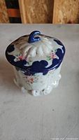 Porcelain container with blue floral pattern and blue rim, showing the top and side details of the lid and container body.