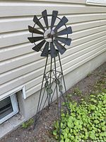Full view of black metal garden windmill standing outdoors next to a house.