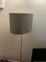 Front view of the floor lamp showing the textured grey woven fabric lampshade and chrome pole with base