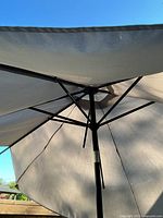 Underside view of beige fabric patio umbrella canopy and metal frame showing broken arms.