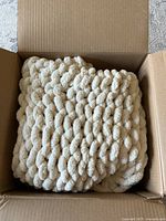 Cream colored chenille blanket folded inside a box showing its chunky knit texture and plush material.