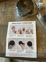 Photo showing black plastic suction hooks components in plastic packaging and installation instruction sheet with step-by-step images.