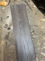 Close-up of a single gray vinyl floor plank showing detailed wood grain texture and finish.