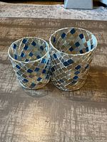 Small and medium-sized diamond mosaic glass and tile candle holders showing blue, silver and clear diamond pattern design arranged together on a textured brown surface.