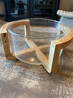 Glass bowl with wide circular shape on curved wooden stand from a top and side angle, showing the minor scratches on the glass and the natural wood grain of the stand.