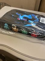 Side view of the binder in plastic packaging showing the multicolor fantasy creature faces on the side.