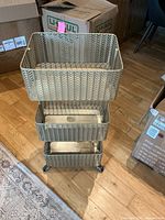 Front view of gold-colored three-tier metal storage cart, showing all three basket tiers and caster wheels.