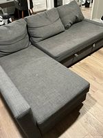 Sectional sofa angled view showing chaise lounge on left side and seat cushions with multiple back cushions, upholstered in medium gray fabric on wood flooring.