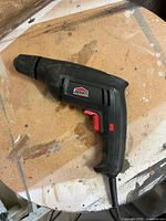 Left side view of the black Jobmate corded electric drill with visible red trigger and keyless chuck, showing some dust and wear.
