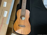 Wooden Kmise ukulele inside a black padded carrying case.