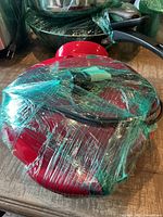 Red electric quesadilla maker wrapped in plastic, showing power cord and indicator lights on top.