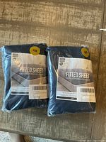 Two dark blue Utopia Bedding fitted sheets in original plastic packaging on wooden surface.