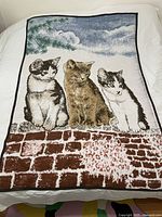 Full view of the woven blanket showing three cats sitting on a brick wall under blue sky.