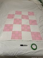 Full view of the handmade quilt laid flat showing a checkerboard pattern with pink solid, pink gingham, and white blocks. Measuring tape shown for scale.