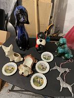 Overview of dog-themed ceramics and pewter decorations on a black table in a workshop or storage area.