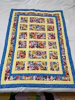 Full view of the handmade lap quilt laid flat showing floral patchwork squares bordered by yellow and blue strips.