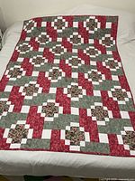Full view of the handmade quilt laid flat showing the complete block design and colors - red, green, white, and strawberry patterned fabrics.