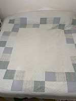 Full view of the blue and white patchwork quilted bedspread showing central white area surrounded by patchwork squares on a bed.