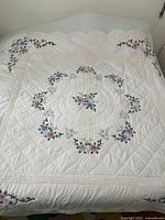 View of full bedspread spread out showing central floral circular pattern, quilting pattern, and scalloped edges with embroidery