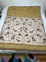 Blanket laid flat showing beige front side with brown floral swirl pattern and mustard yellow circular border section