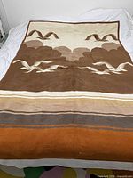 Full view of the vintage seagulls blanket laid on a bed, showing the brown and cream color scheme with seagulls flying along the middle and horizontal stripes at the bottom edge.