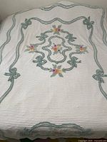 Full view of the cream chenille bedspread with green scrolls and multicolor floral embroidery spread on a bed.