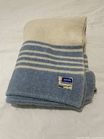 Folded view of vintage Eaton wool blanket showing blue and cream stripes and Eaton label.