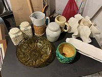 Overview of all items on table showing salt and pepper shakers, ceramic jug and container, green bowl, yellow glass bowl, mug, corn dishes, and candle holder.