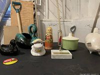 Overview of the vintage lot showing all items: BMP green swan planter, black duck figurine, white duck flower frog, Russian nesting doll, green pot with lid and spoon, and ceramic piggy banks.