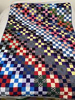 Full view of the vintage handmade patchwork quilt spread out on a bed showing colorful checkerboard pattern squares.