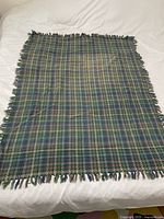 Top-down view of the full woven blanket laid flat on a white surface, showing plaid pattern and fringed edges.