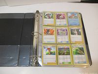 Open binder showing a page of Pokémon trainer and item cards in plastic sleeves, arranged 3 cards wide and 3 cards tall.