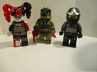Front view of three LEGO minifigure clocks: Harley Quinn, dinosaur, ninja.