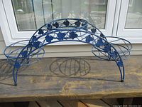 Metal plant stand with three circular pot holders arranged in a triangular formation, blue painted metal with leaf accents on the arch frame