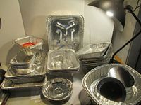 Photo showing a pile of assorted aluminum baking pans including rectangular, square, round pans, and pans with specialty shapes, all new and unused.