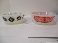 Two white glass bowls with floral exterior patterns, side by side on a white surface against a white background.