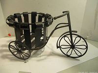 Side view of black metal bicycle planter showing structure, wheels, and open basket