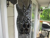 Front angle of black cast iron owl candle holder hanging outdoors on a porch with detailed owl features visible.
