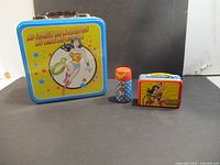 Front and side views of the metal lunch box and Wonder Woman salt and pepper shakers with a small matching tin case
