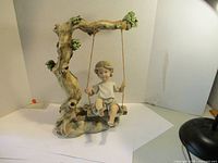 Front and slightly angled view of the entire garden ornament, showing the child on the swing and twisted tree branch with foliage
