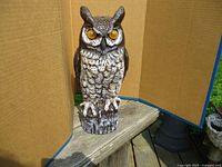 Front view of plastic garden owl statue on wooden surface with cardboard background