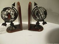 Pair of metal globe bookends with wooden bases and upright wooden support, showing front and side details including arrow on globe.