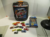 Front view of Hot Wheels 100 Car Case with 13 assorted loose Hot Wheels cars displayed in front and unopened Billboard Car in blister pack.