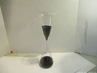 Front angled view of the hourglass showing black sand in the upper bulb beginning to flow downward.