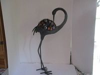 Front view of the metal bird sculpture showing the curved neck and glass-like circular accents on the body.