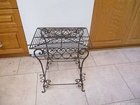 Front side view of the metal table showing detailed scrollwork and curved legs.