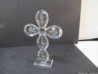 Front view of the clear crystal glass cross showing teardrop-shaped arms, central square block, and rectangular base.